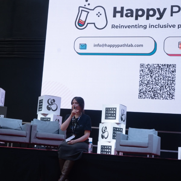 HappyPathLAB speaker on stage at a conference, with the HappyPathLAB logo on the screen behind